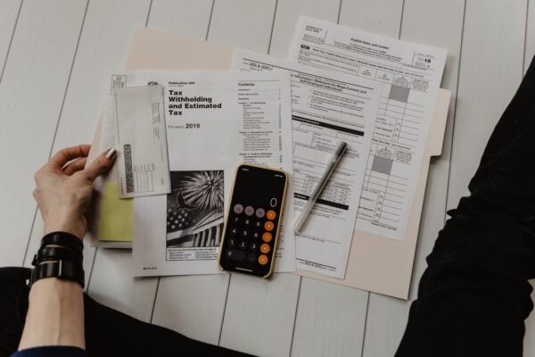 person holding paper near pen and calculator